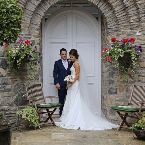 Bride and groom standing in a stone archway with hanging flower baskets.