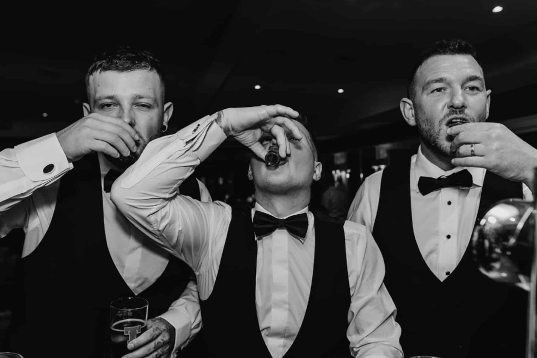Three men in formal attire take shots at a bar.