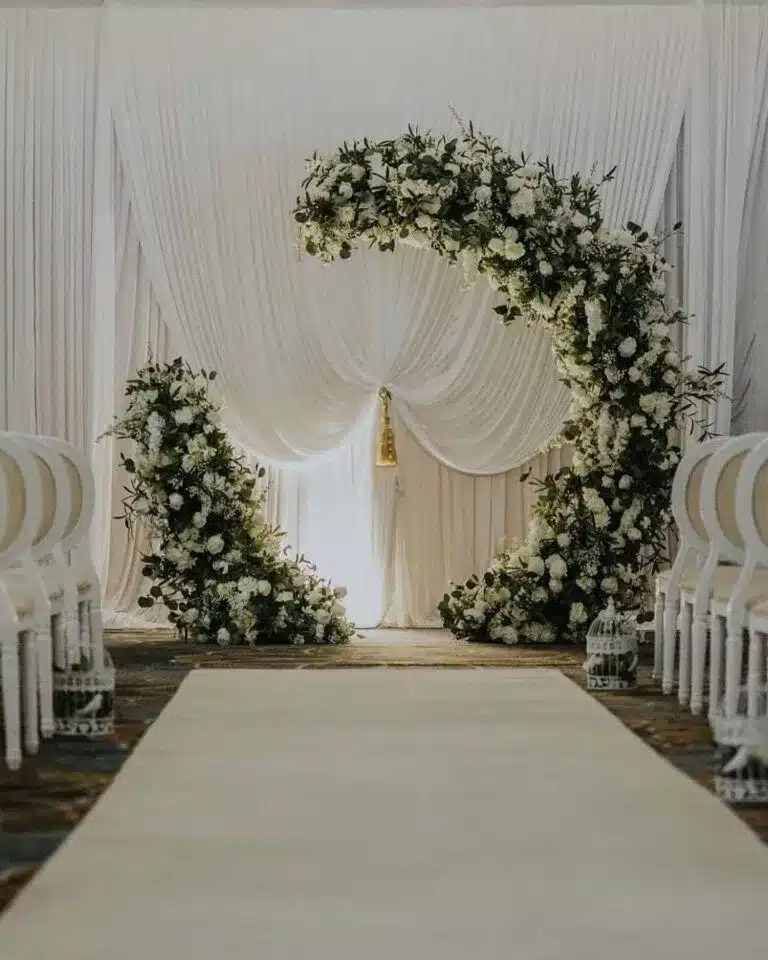 Floral wedding ceremony backdrop with draped fabric and arch, featured in vendor listing card.