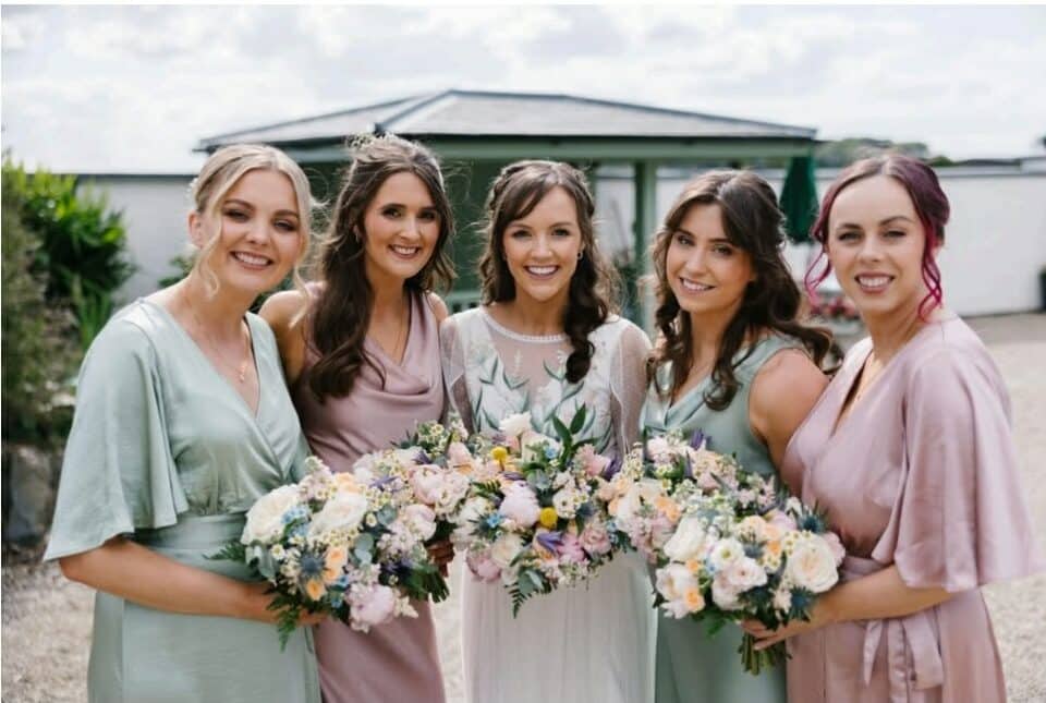 Bride with four bridesmaids holding bouquets, smiling outdoors.