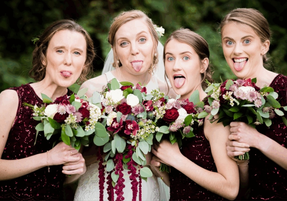 Bride and bridesmaids with burgundy bouquets making funny faces.