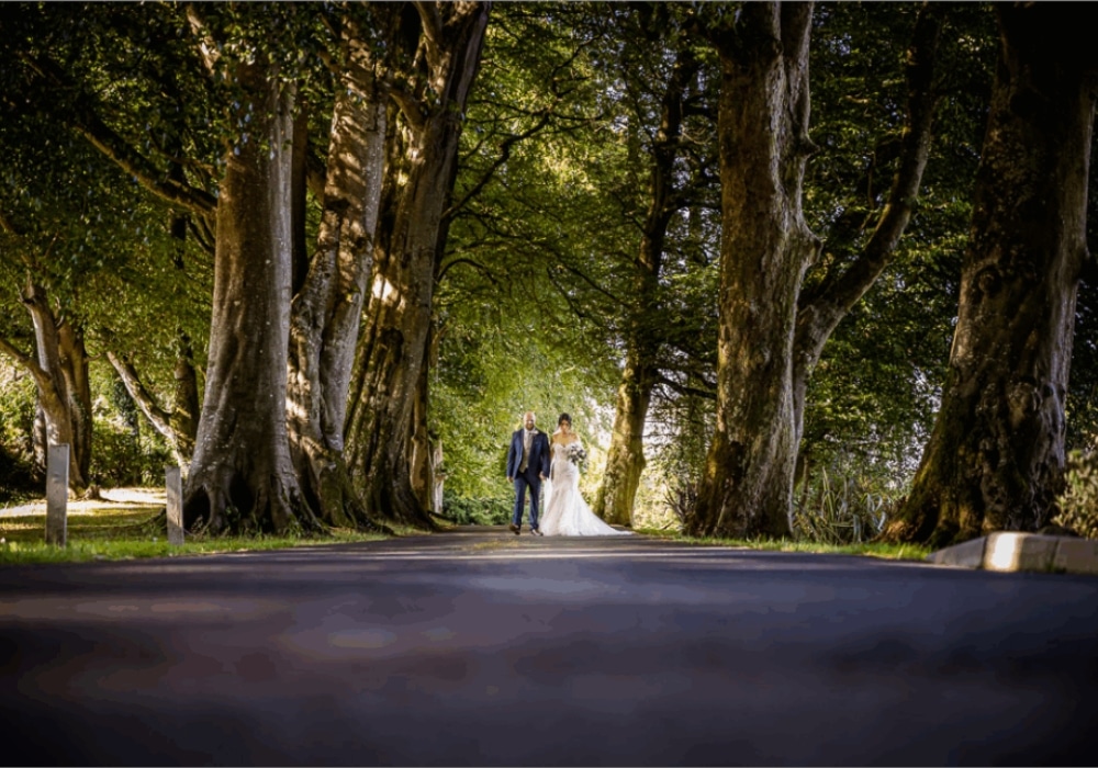 Bride and groom walking down a tree-lined path.