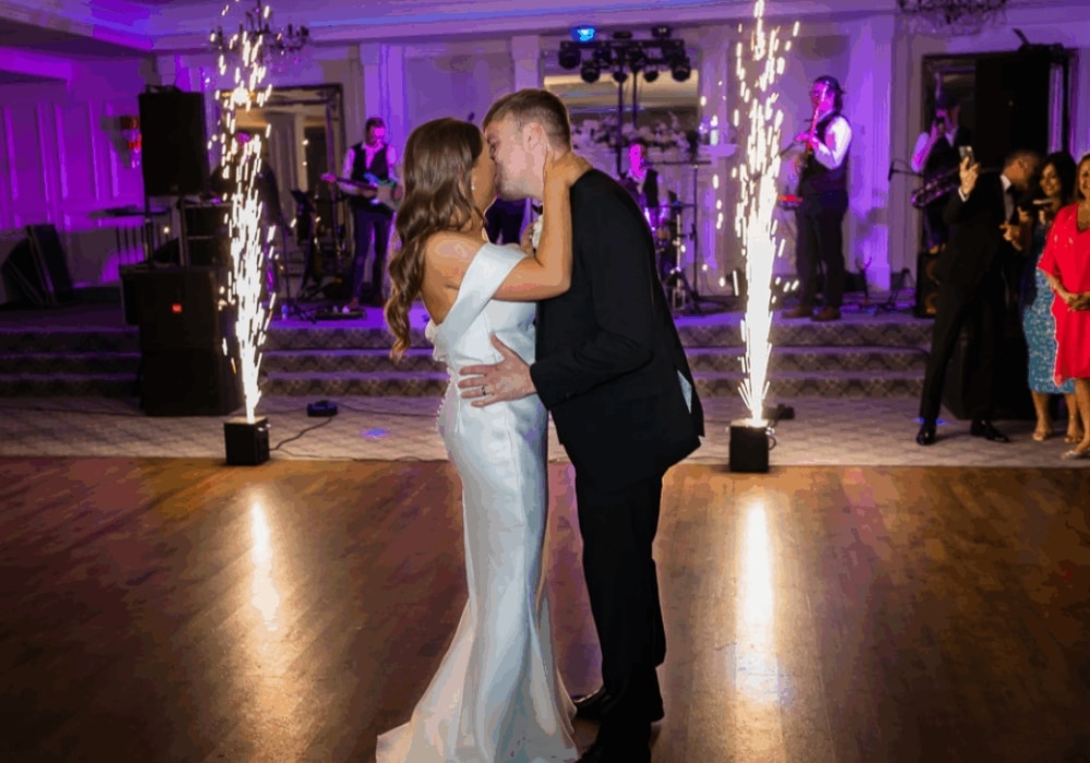 Couple kissing on dance floor with sparklers and live band in background.