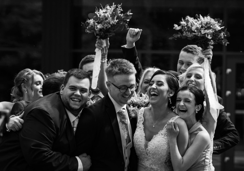 Group of people celebrating at a wedding, smiling and holding flower bouquets.