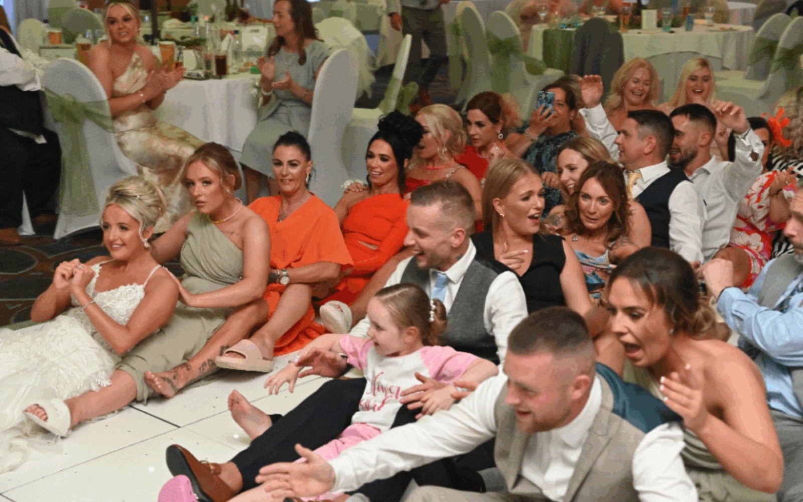 Group of people sitting on the floor laughing and clapping at an indoor event.