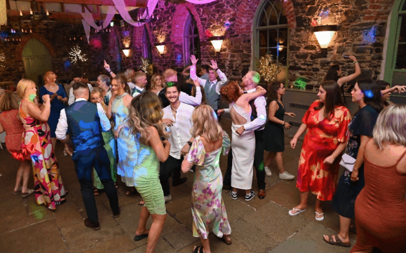 People dancing at a lively indoor party with colorful lights and festive decorations.