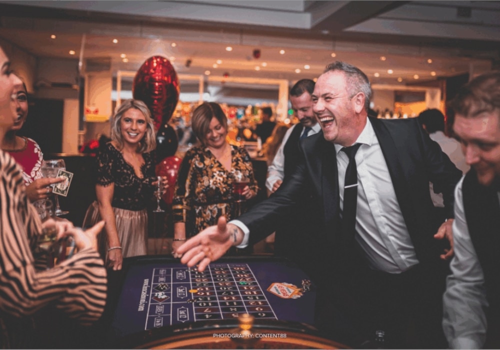 People enjoying a casino-themed party, laughing and socializing around a roulette table.