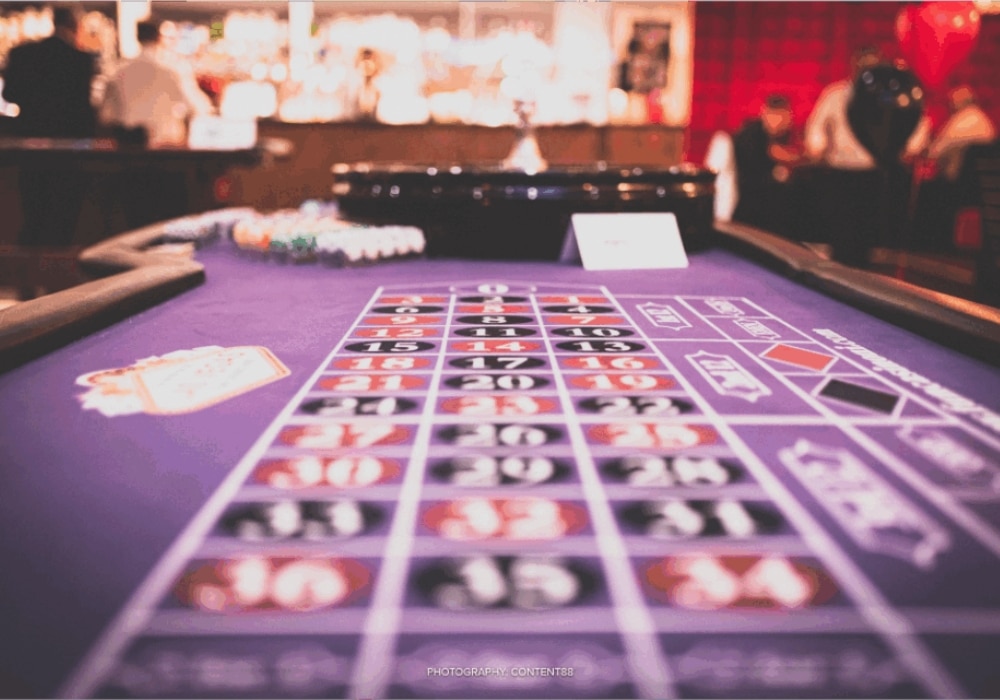 Purple roulette table with numbers and betting areas in a casino environment.