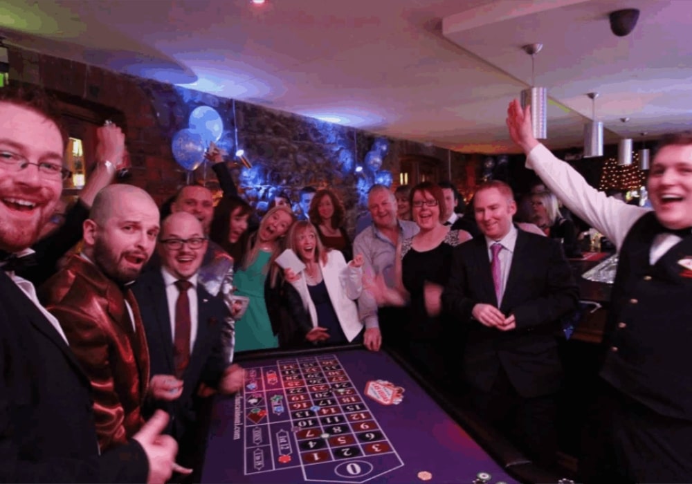Group of people celebrating around a casino roulette table.