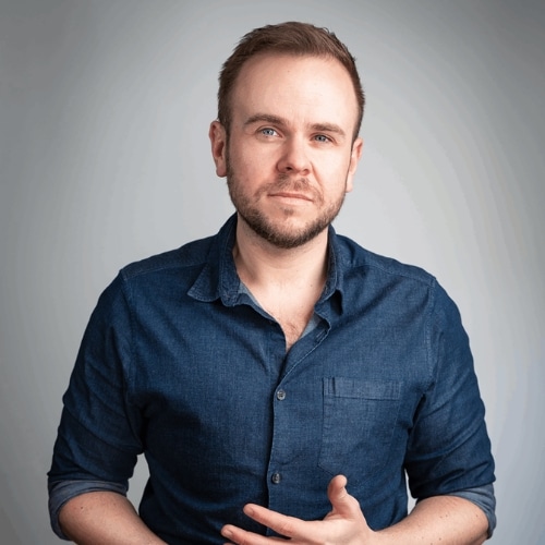 Man in denim shirt with a thoughtful expression against a gray background.