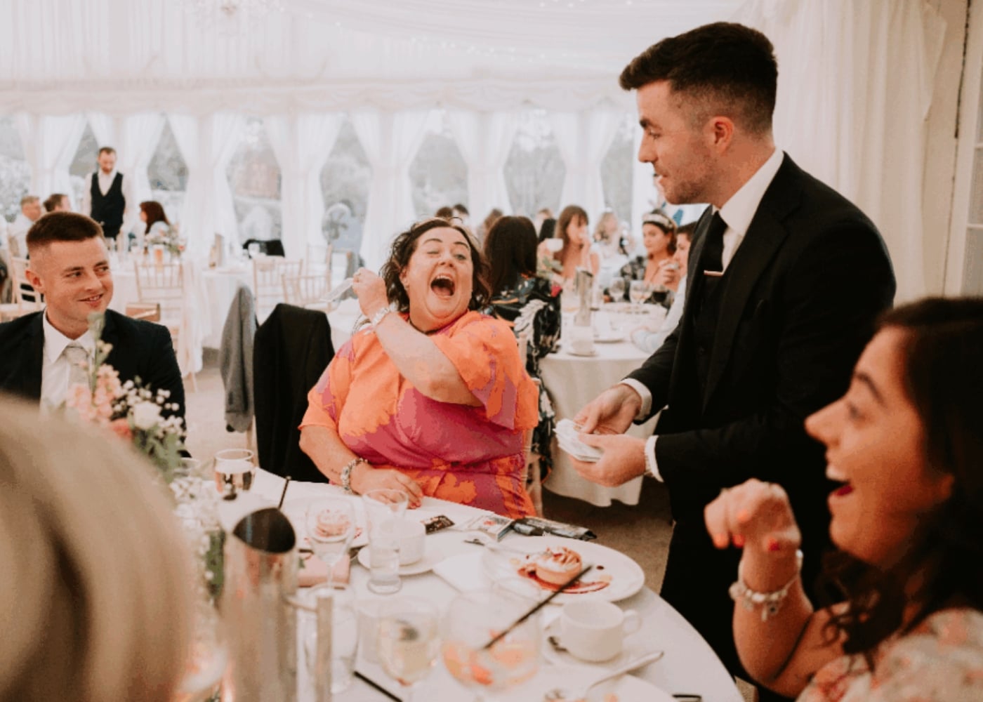 People laughing and enjoying a magic trick at a wedding reception.