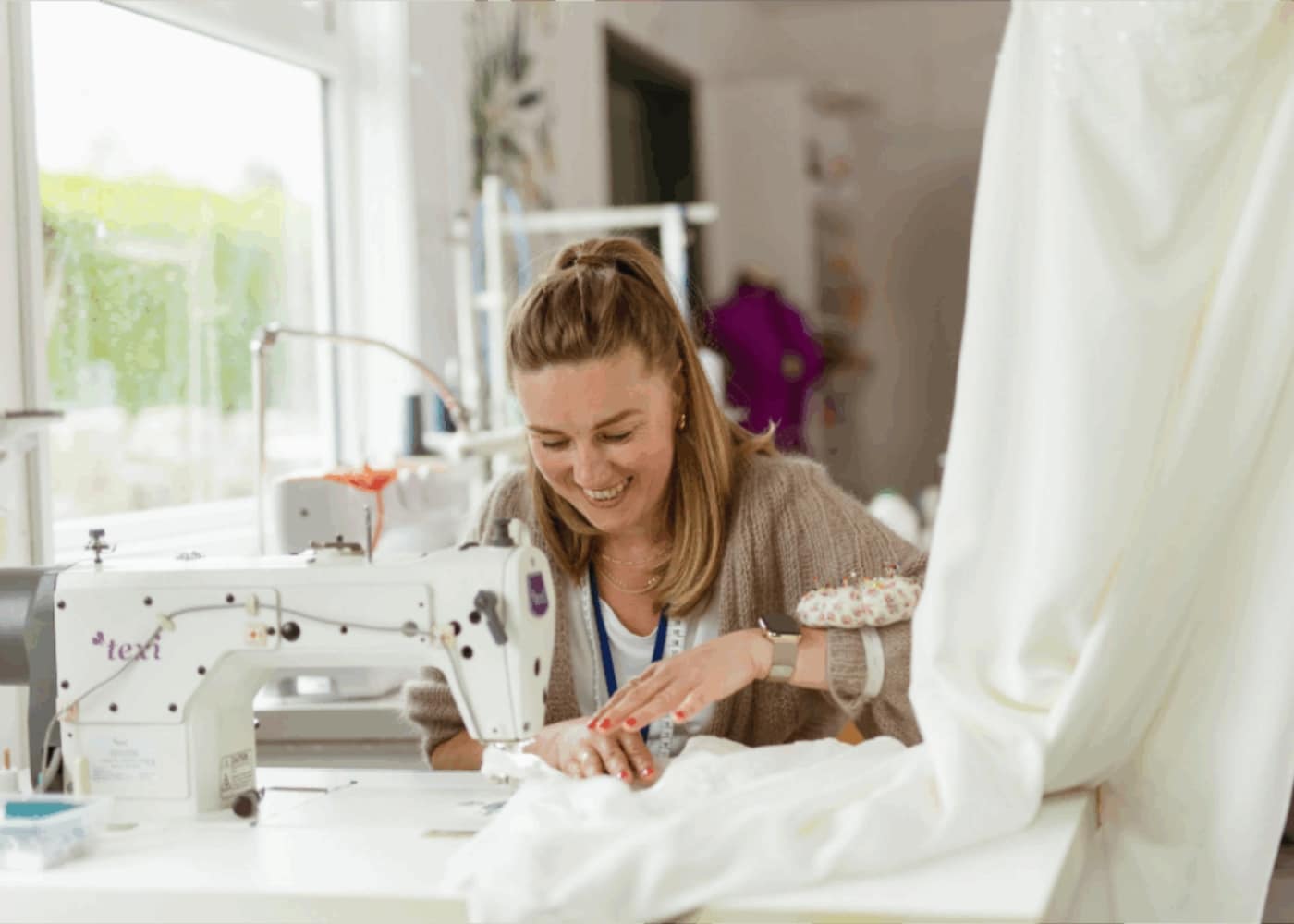 Woman smiling while sewing a white fabric with a sewing machine.