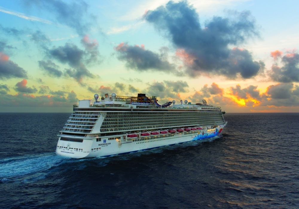Cruise ship sailing at sunset with colorful sky and clouds.