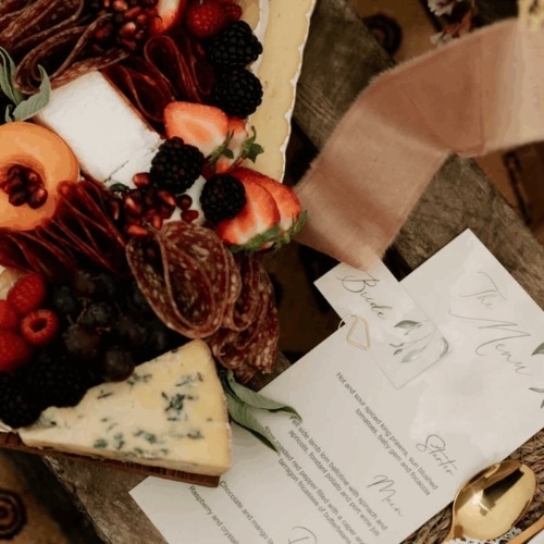 Charcuterie board with assorted cheeses, meats, berries, and a menu card on a wooden surface.