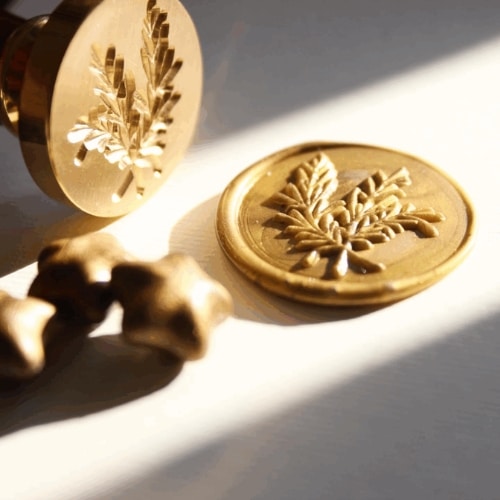 Wax seal stamp with leaf design and wax impressions on a table.
