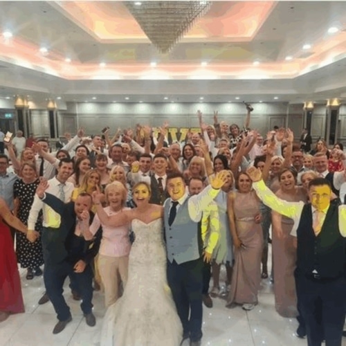 Wedding celebration with a large group of guests, including the bride and groom, posing happily in an elegant venue.
