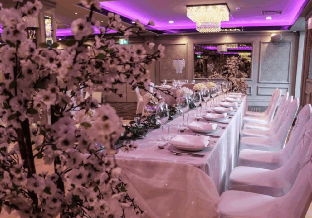 Elegant banquet table with white floral decorations and purple lighting in a luxurious dining room.