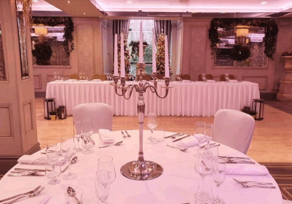 Elegant banquet hall setup with a round table, candelabra centerpiece, and a long table in the background adorned with floral decor.