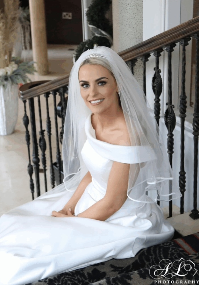 Bride in a white dress and veil sitting on stairs, smiling.