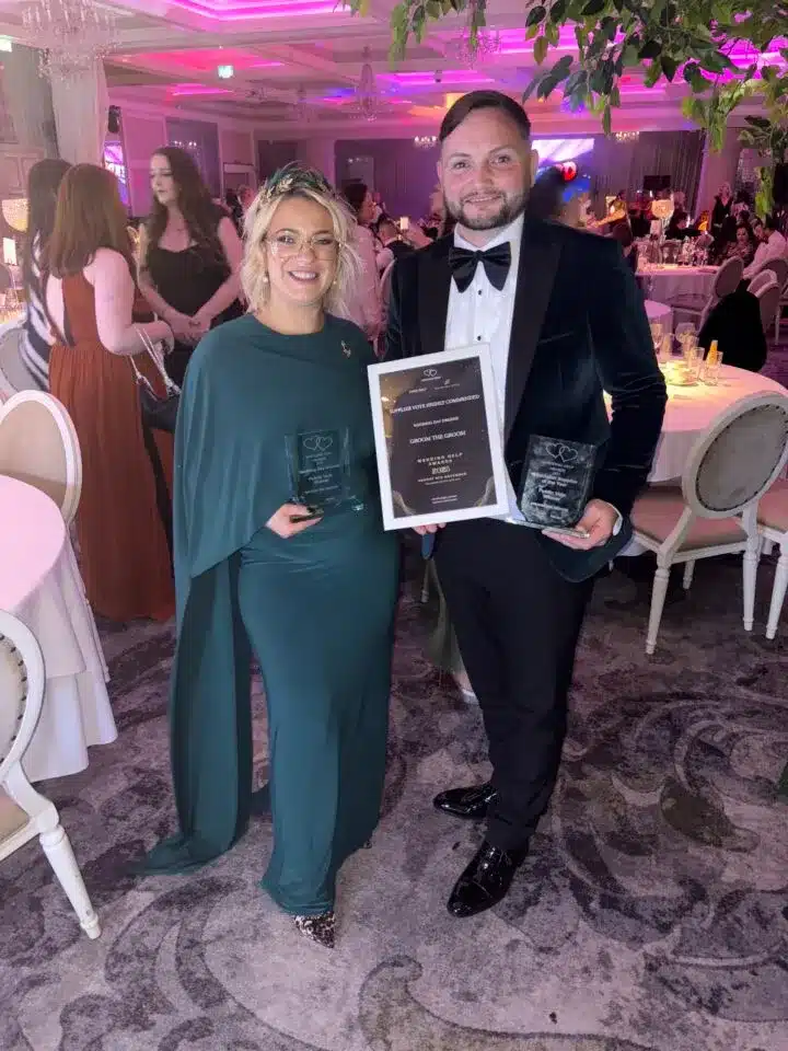 Two guests posing at event, one holding an award plaque.