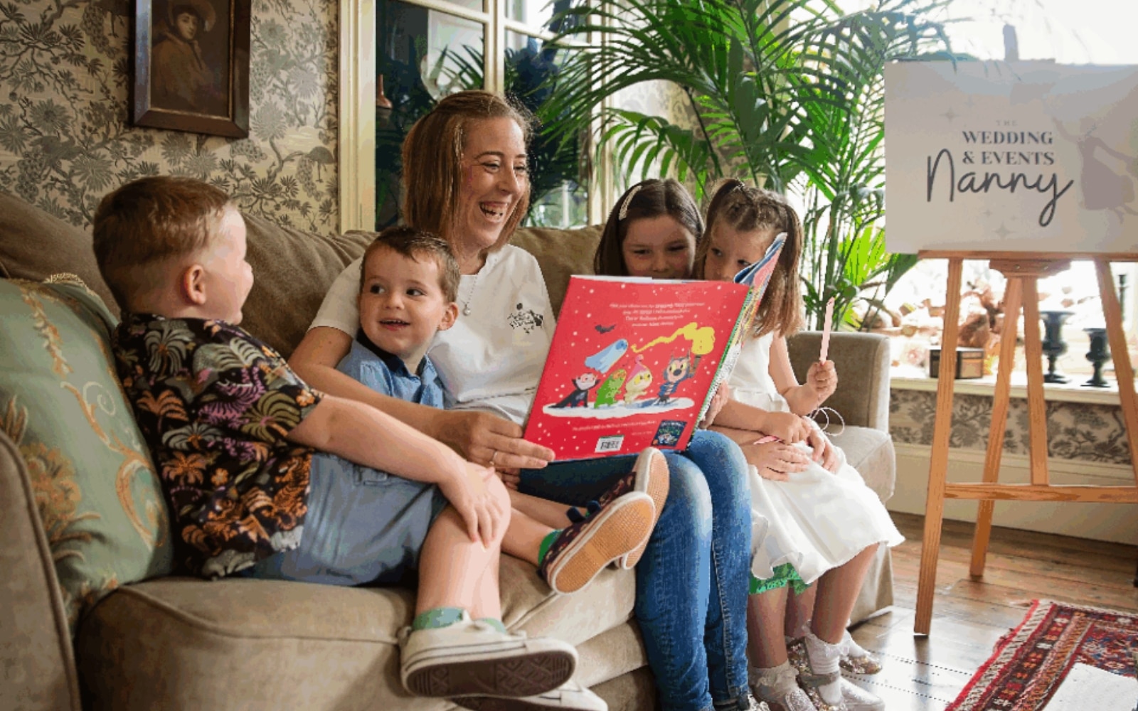 Woman reading a colorful book to four children on a couch, with a "Wedding & Events Nanny" sign nearby.