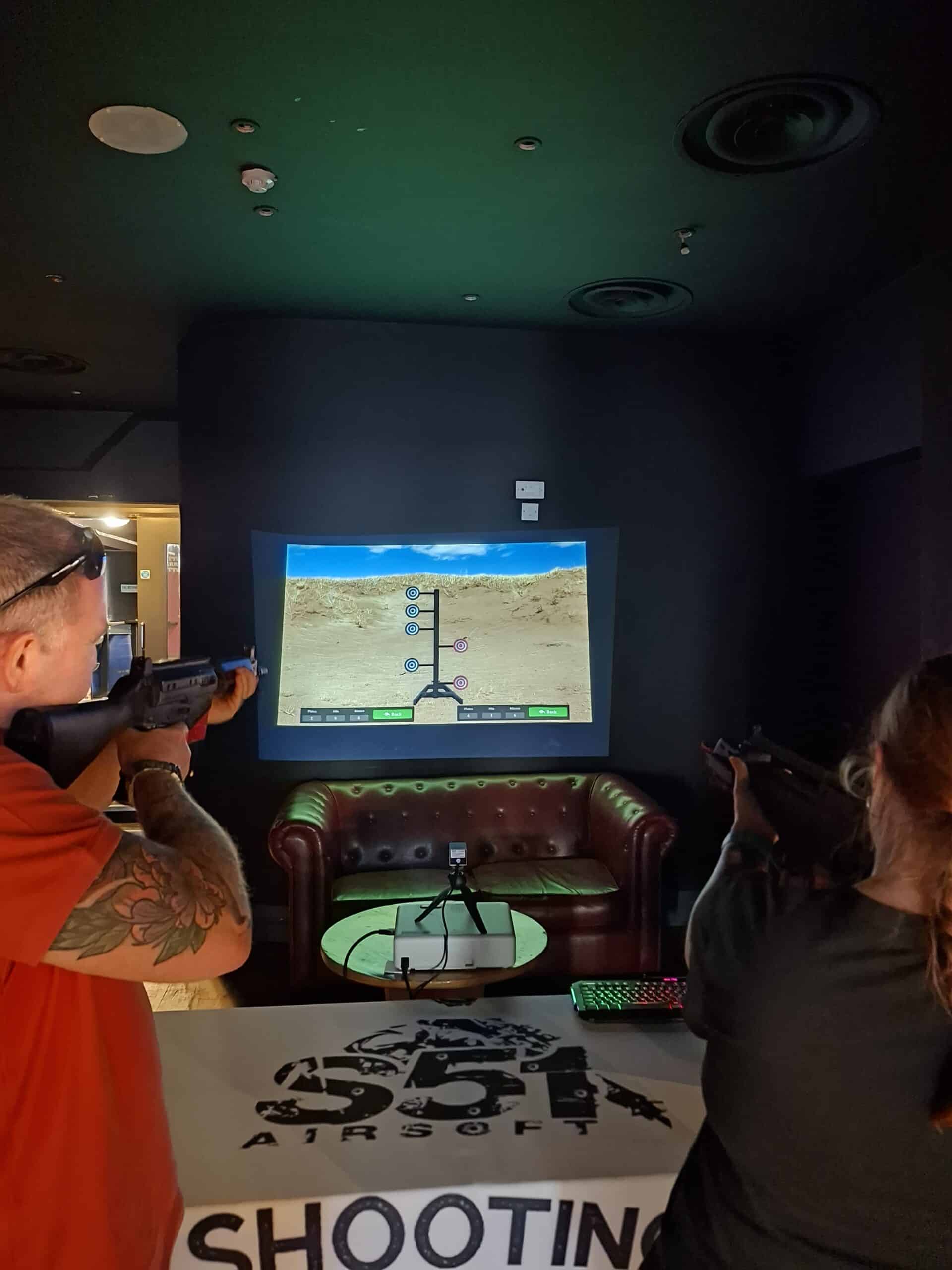 Two people playing an interactive shooting game on a large screen in a dimly lit room.