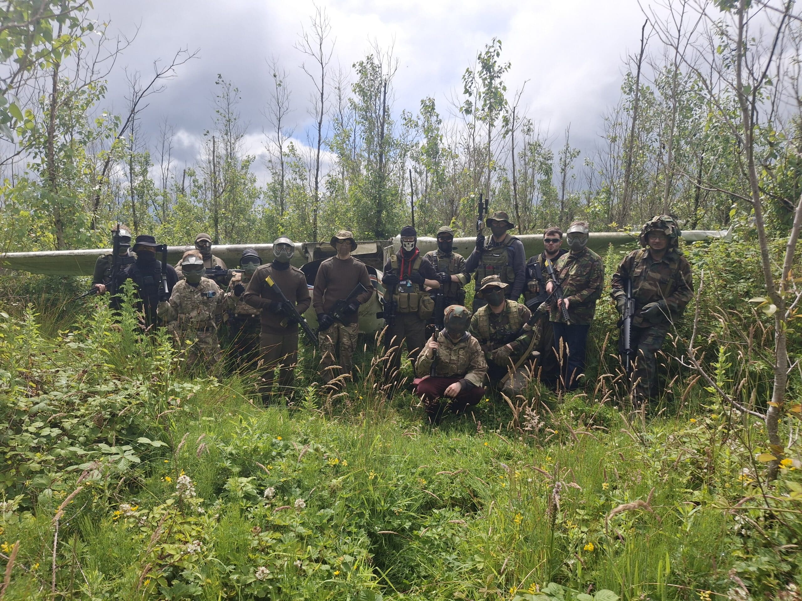 Group of people in camouflage gear holding paintball guns outdoors in a forest setting.