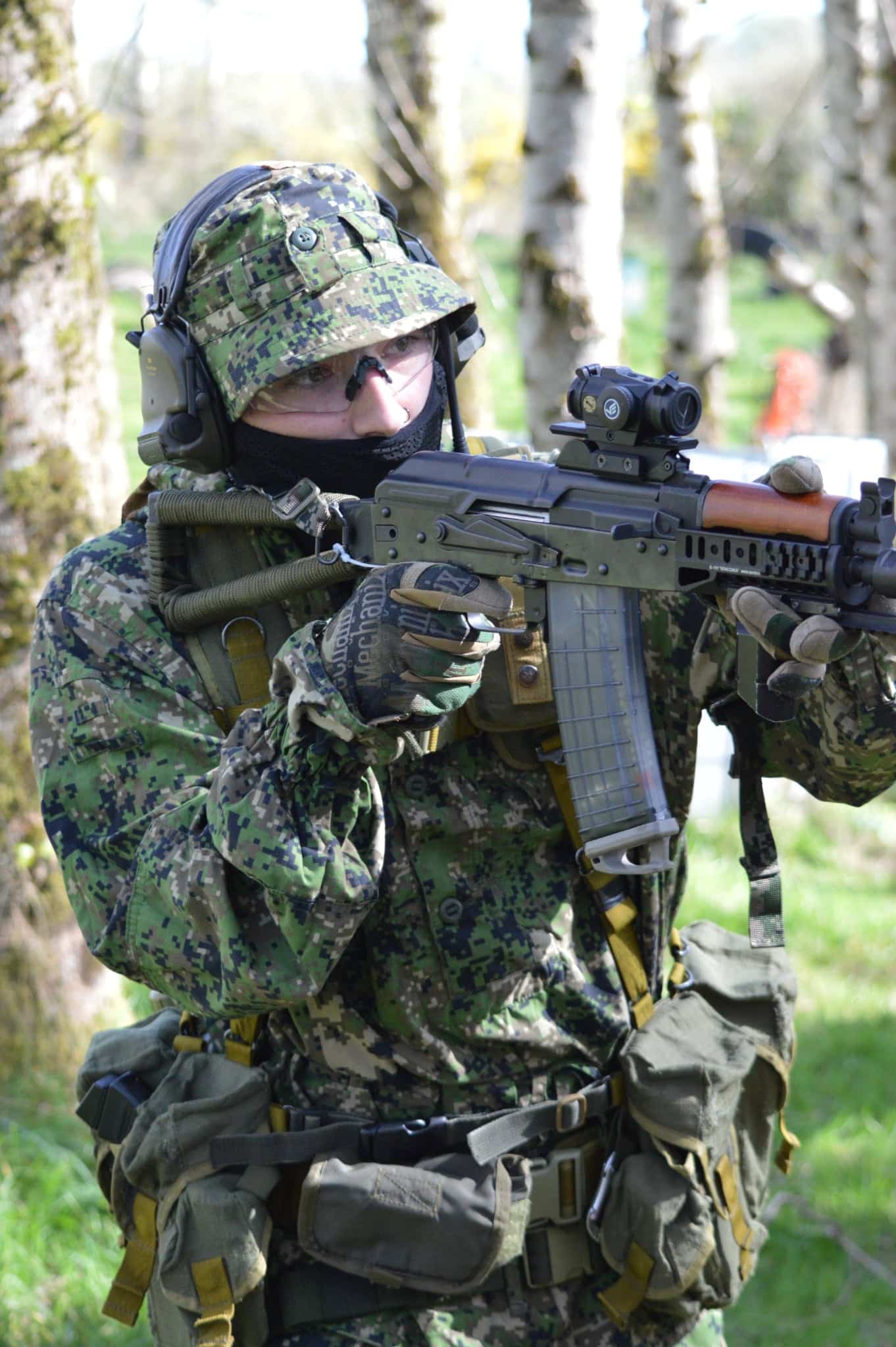 Soldier in camouflage gear aiming a rifle outdoors.