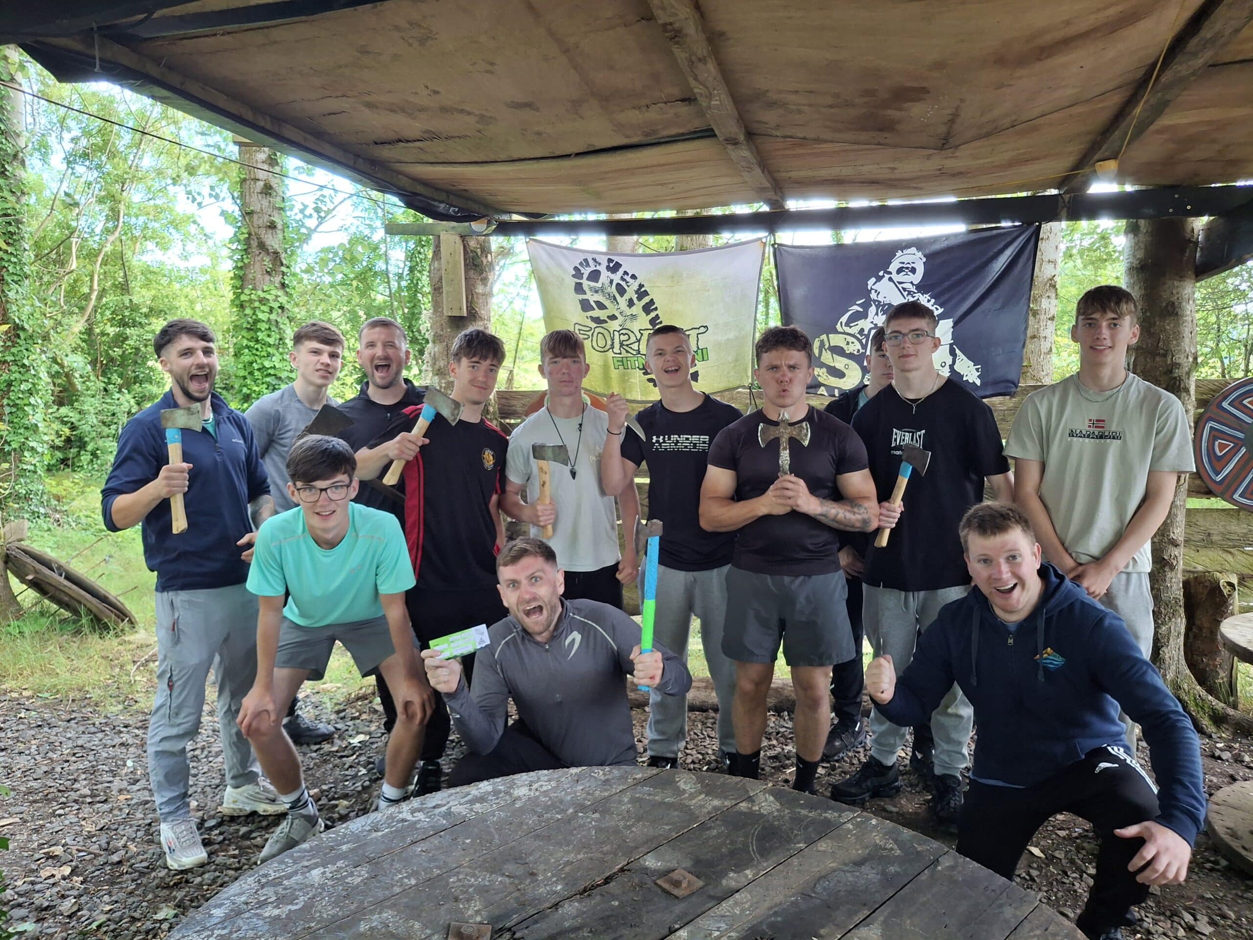 Group of young men holding axes in an outdoor setting with banners in the background.