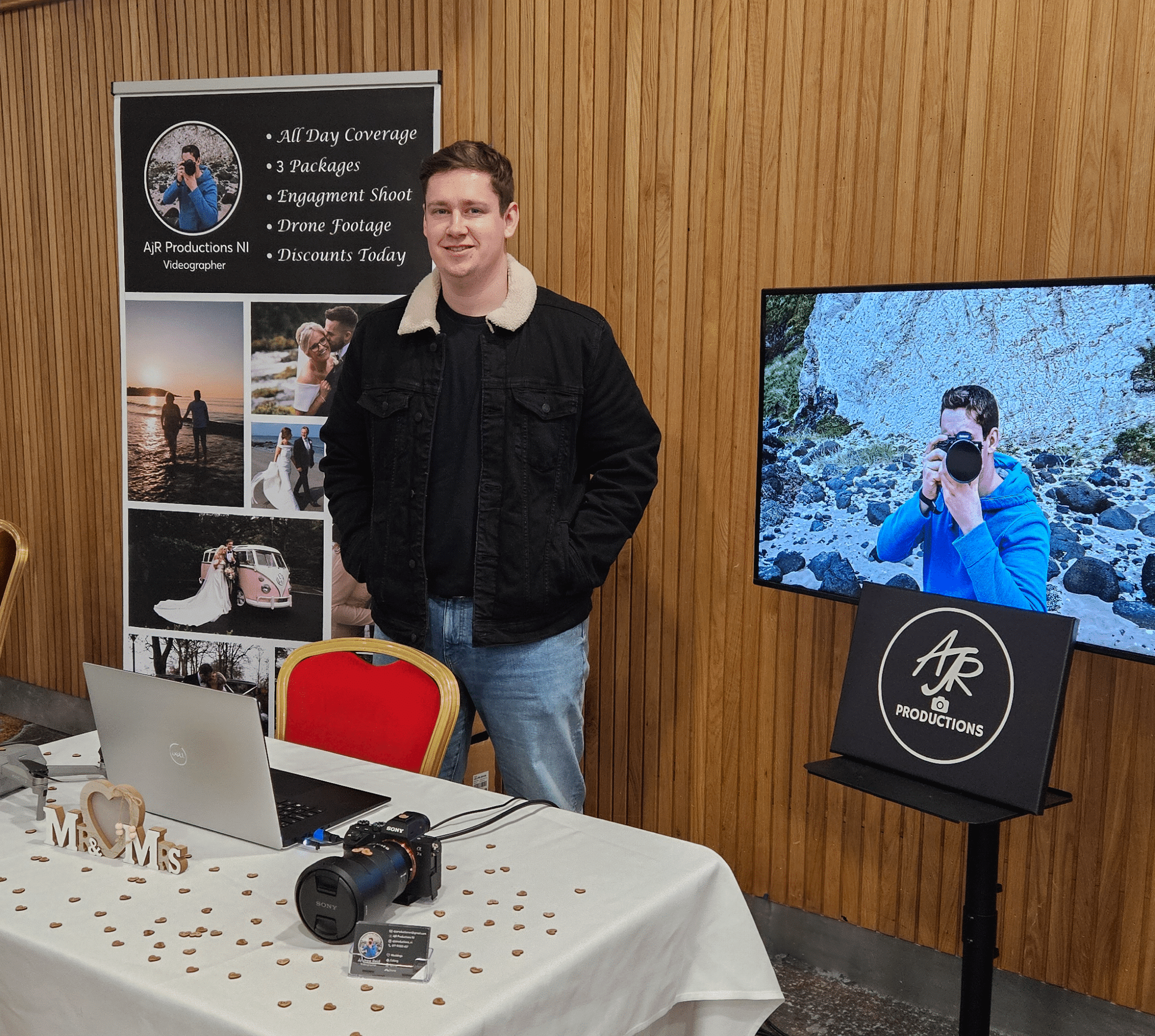Man standing at a wedding videography booth with promotional materials and a camera setup.