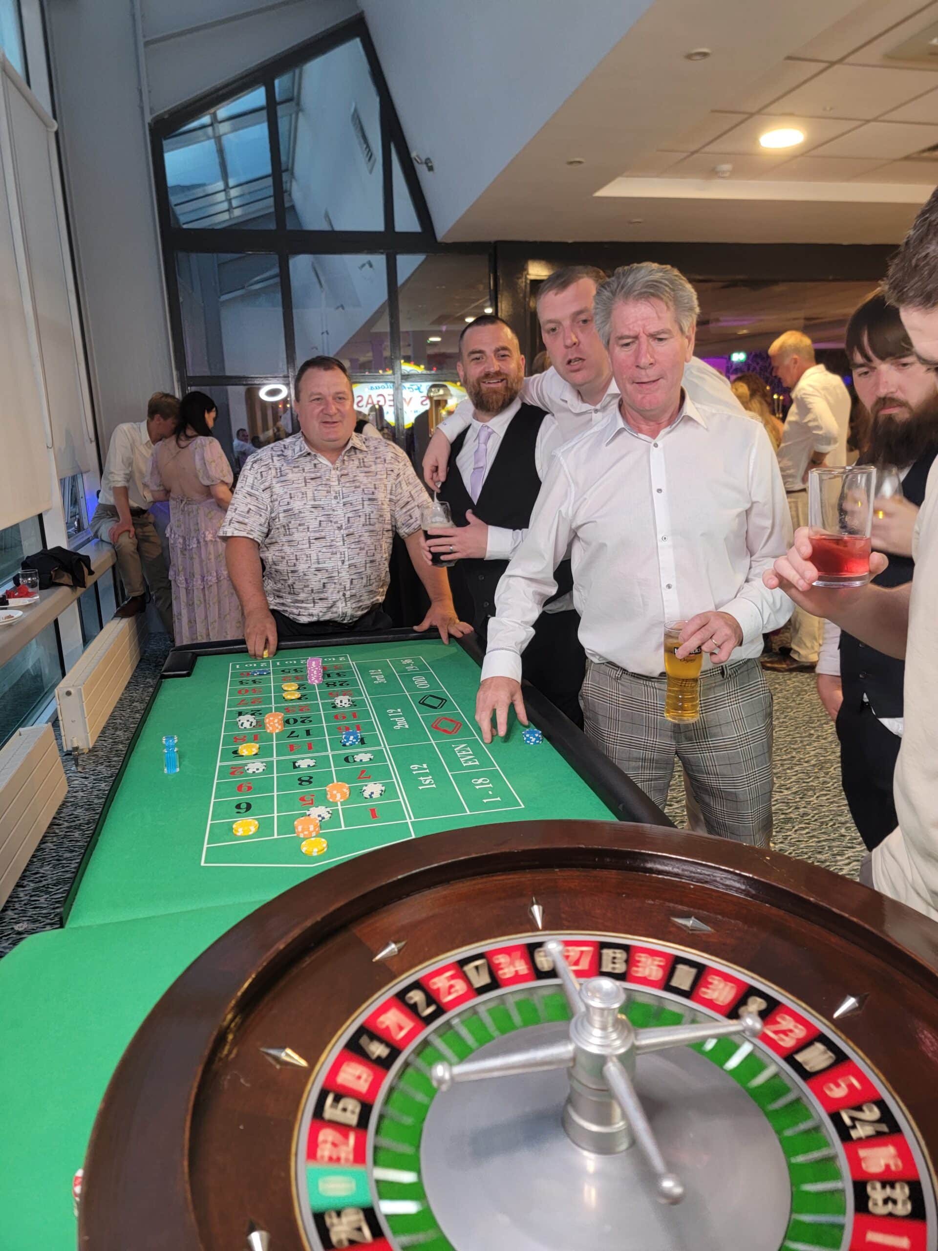Group of people enjoying a night at the casino, standing around a roulette table.