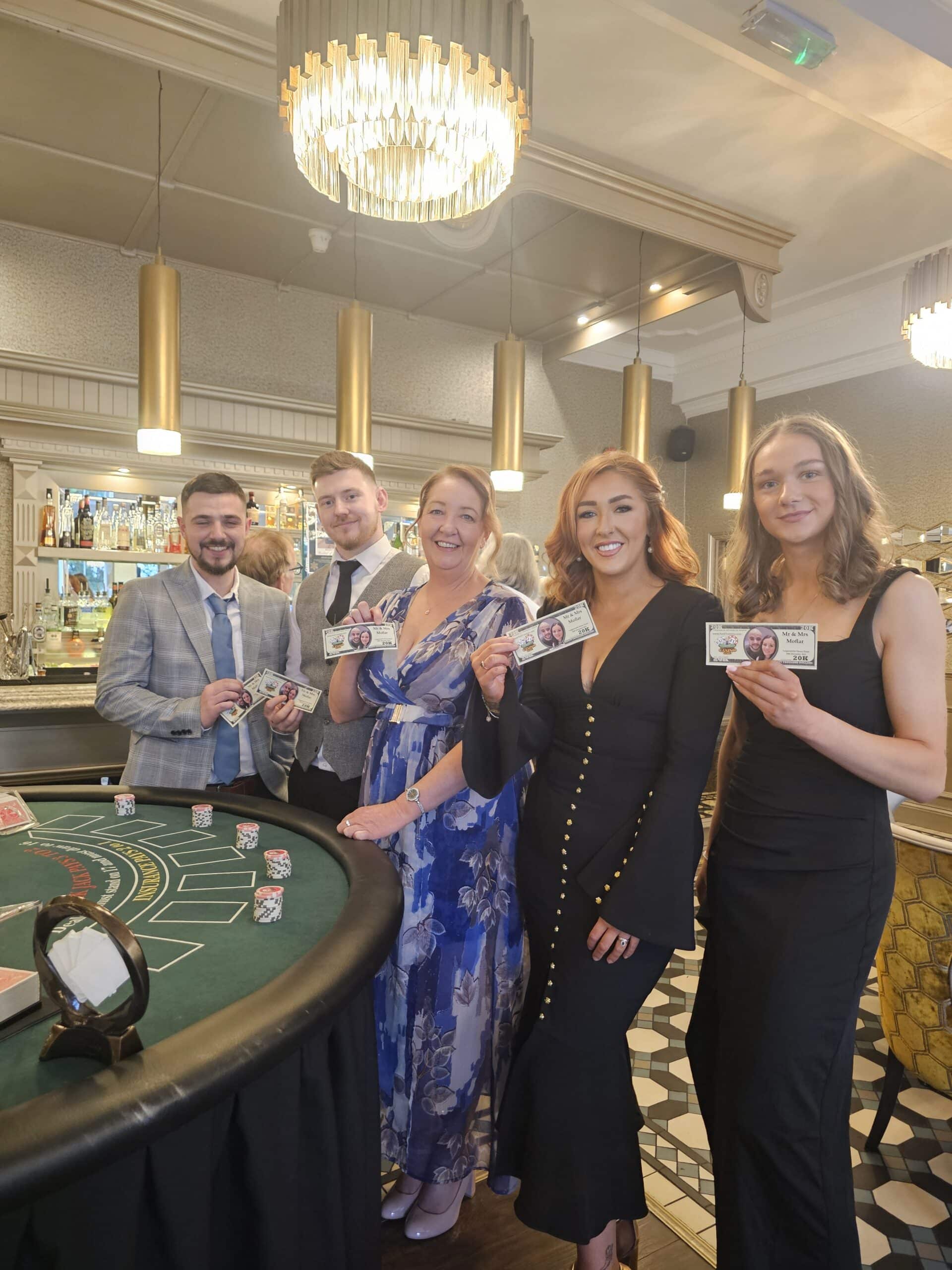 Group of people in evening attire holding novelty money at a casino-themed event.