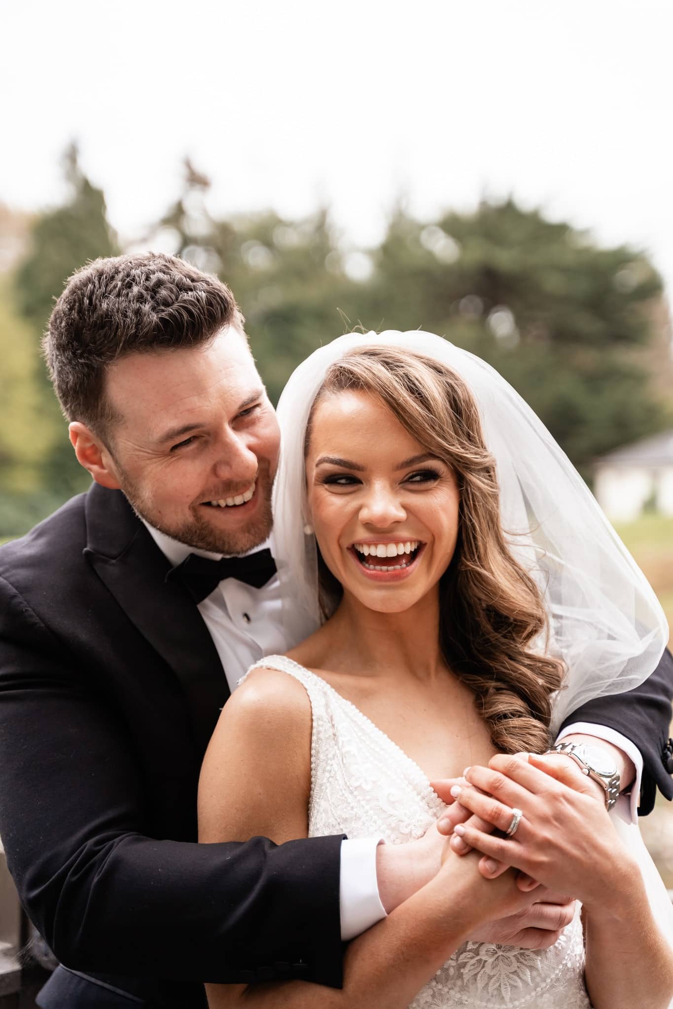Bride and groom laughing and embracing outdoors on their wedding day.