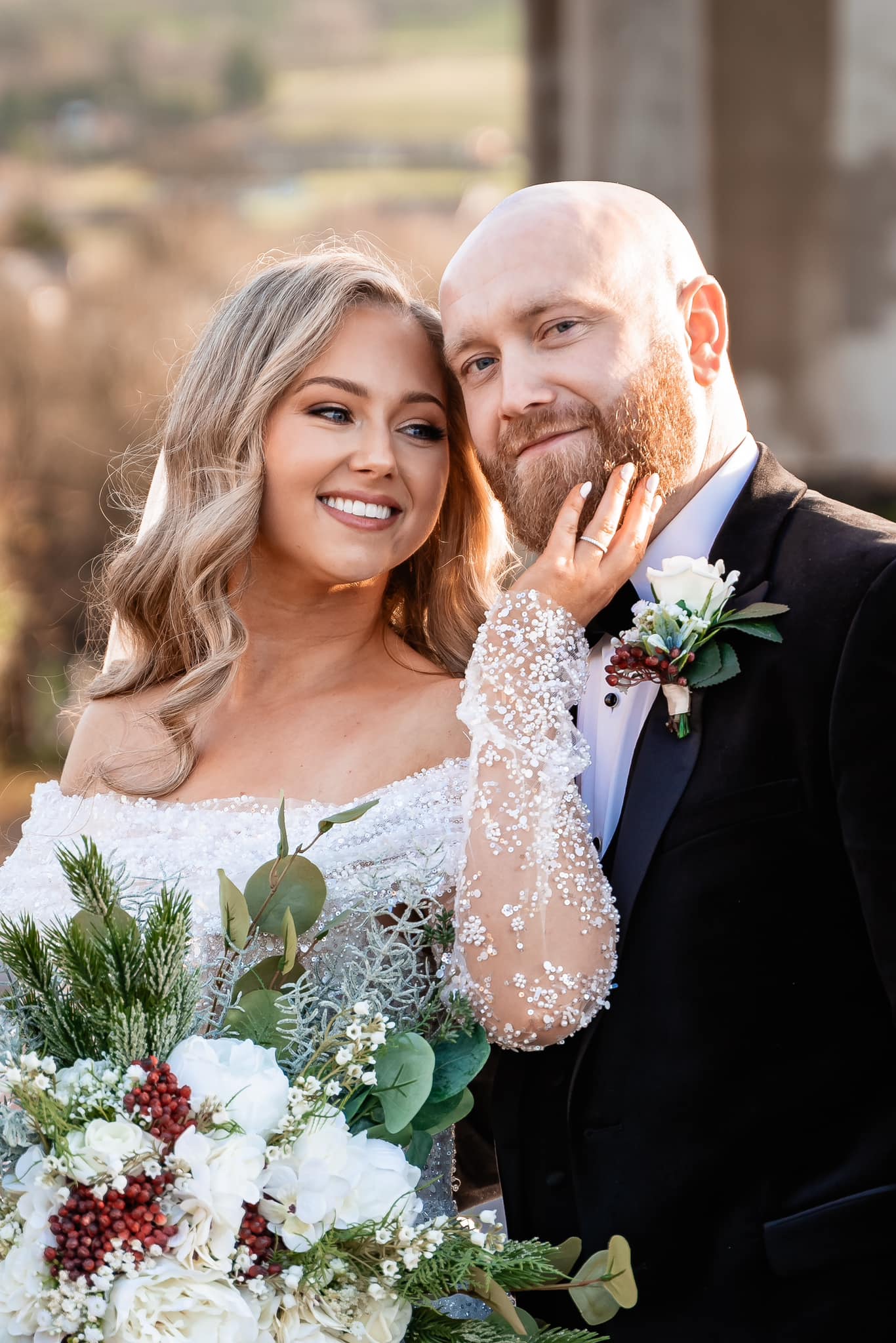 Bride and groom smiling, with a bouquet of flowers, in an outdoor setting.