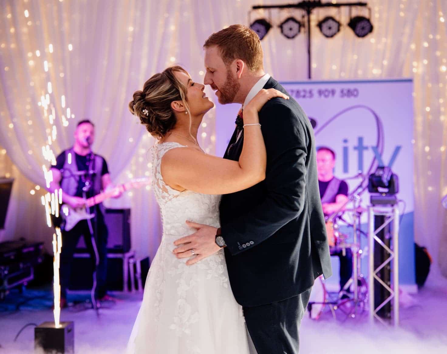 Bride and groom share a dance at their wedding reception with live band and festive lighting.