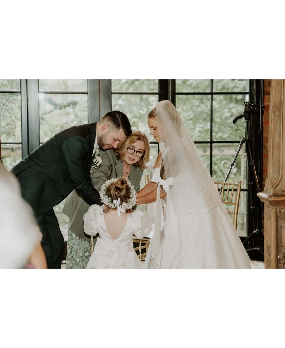 Bride and groom with a guest and flower girl in a white dress during a wedding ceremony.