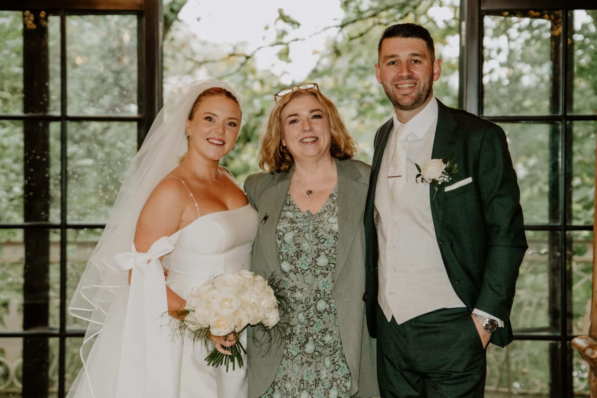Bride and groom smiling with a guest at their wedding, standing indoors.