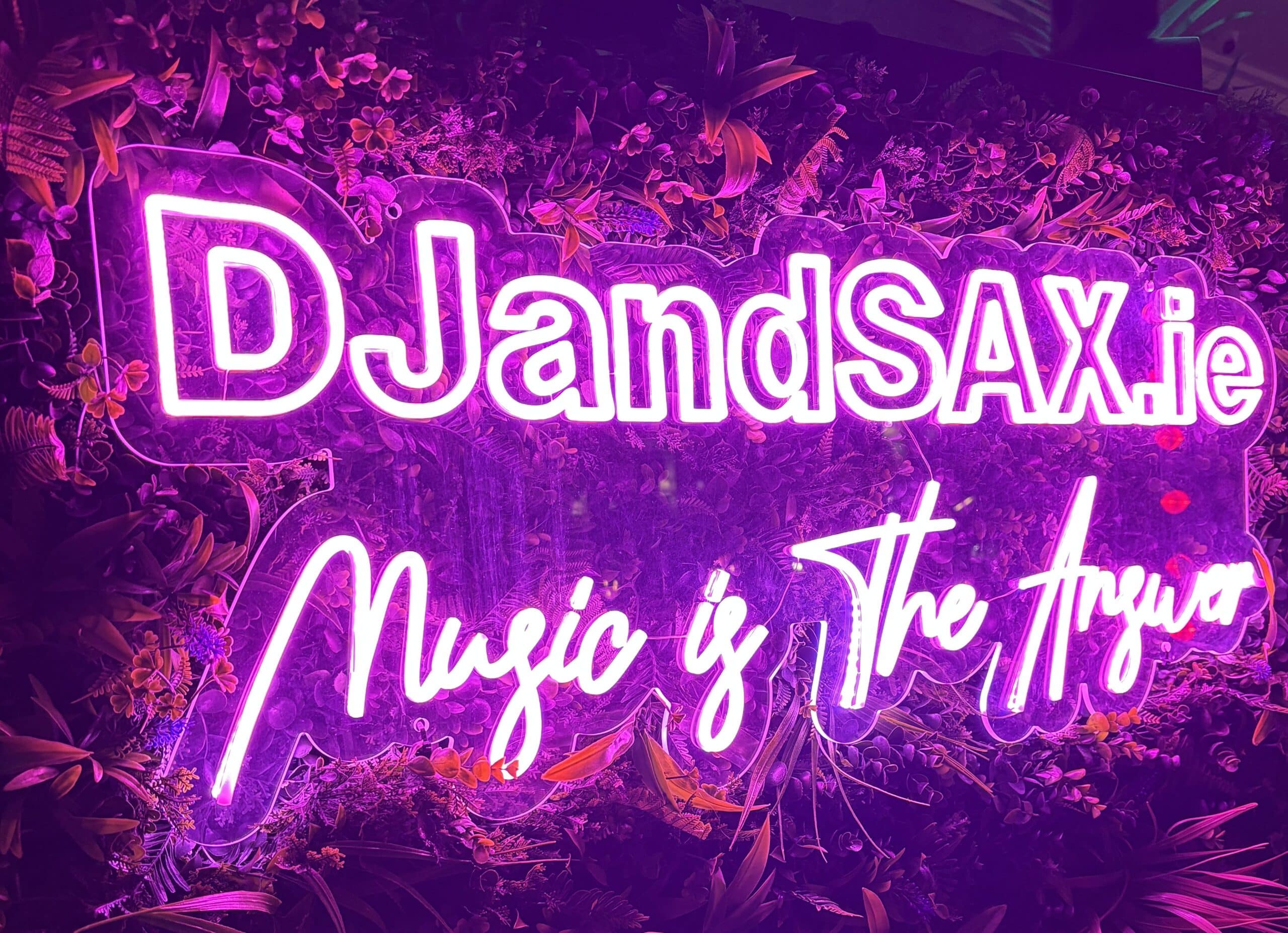 Neon sign reading "DJandSAX.ie Music is The Answer" with floral background.