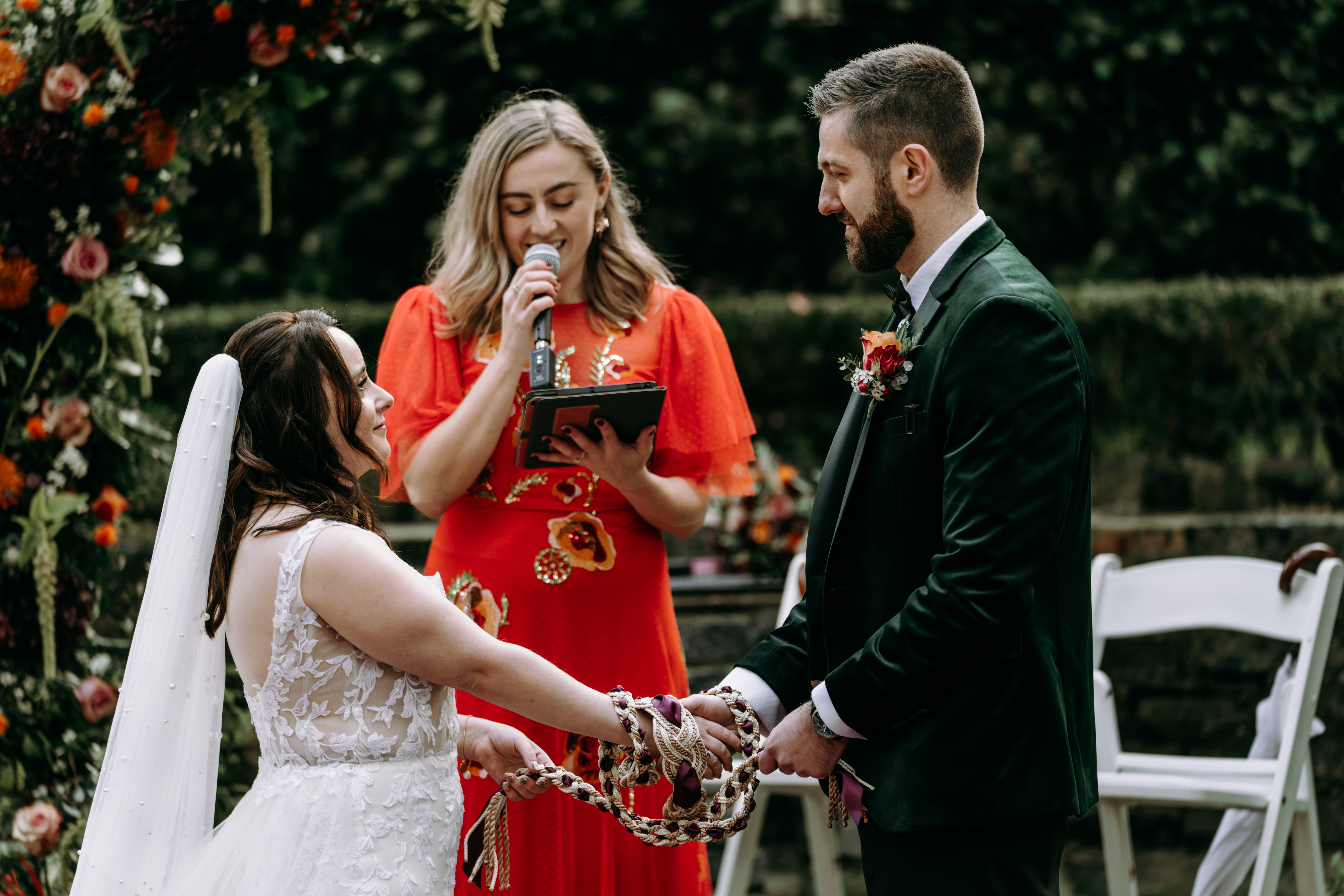 Bride and groom hold hands during a wedding ceremony, with an officiant speaking.