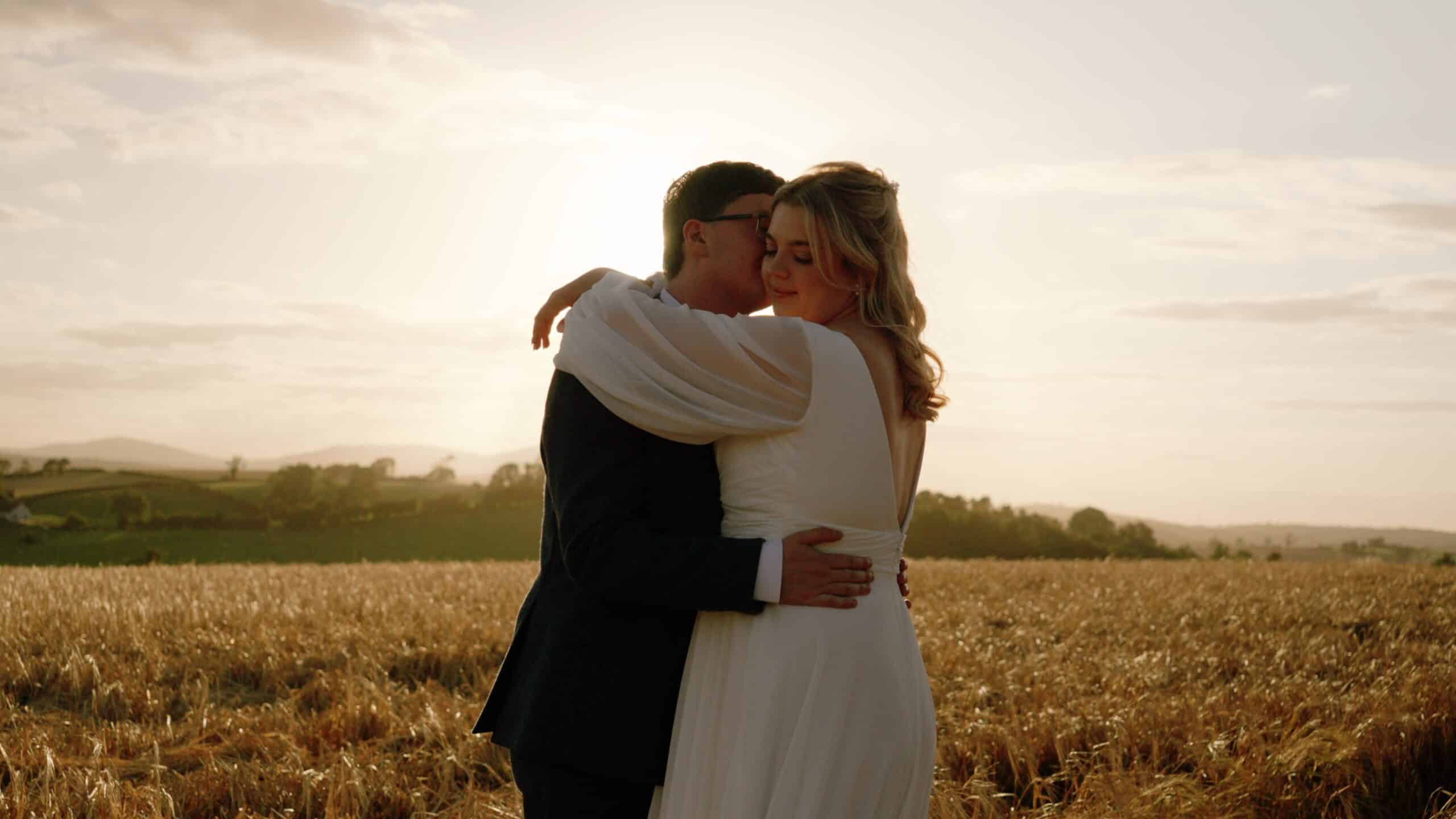 Couple embracing in a sunlit wheat field at sunset.