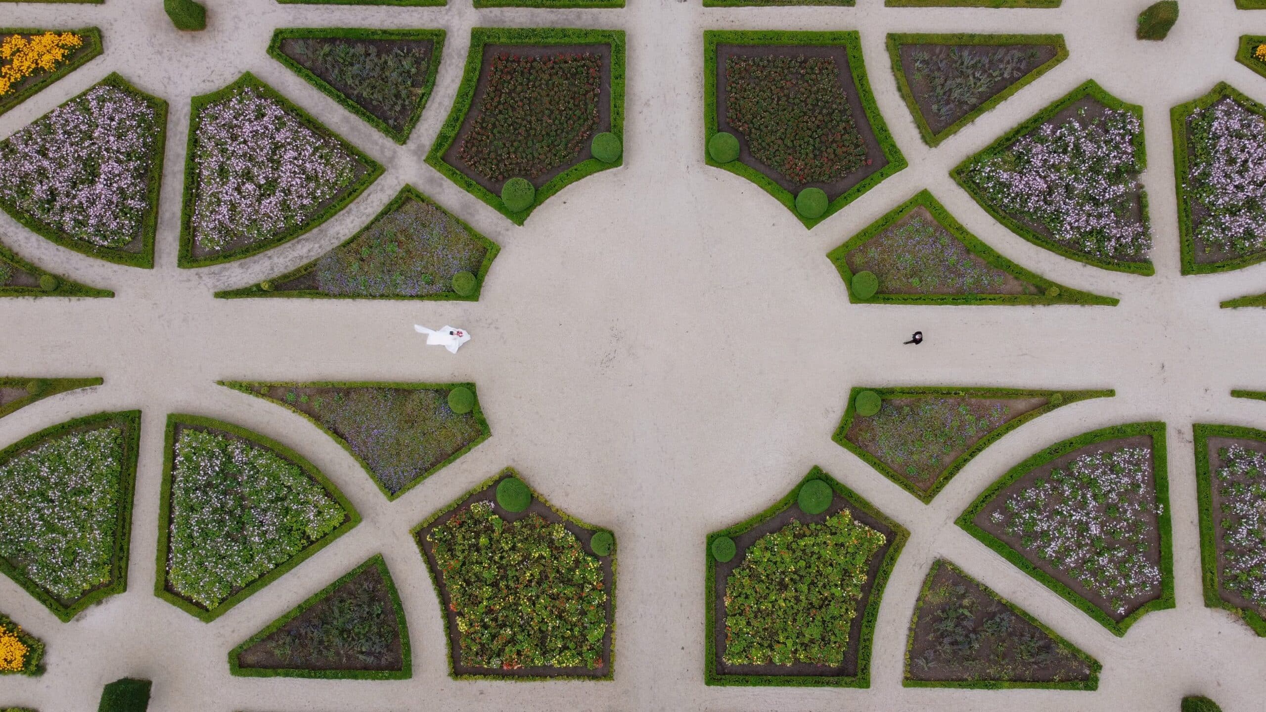 Aerial view of a symmetrical garden with geometrically arranged flower beds and a central circular pathway.