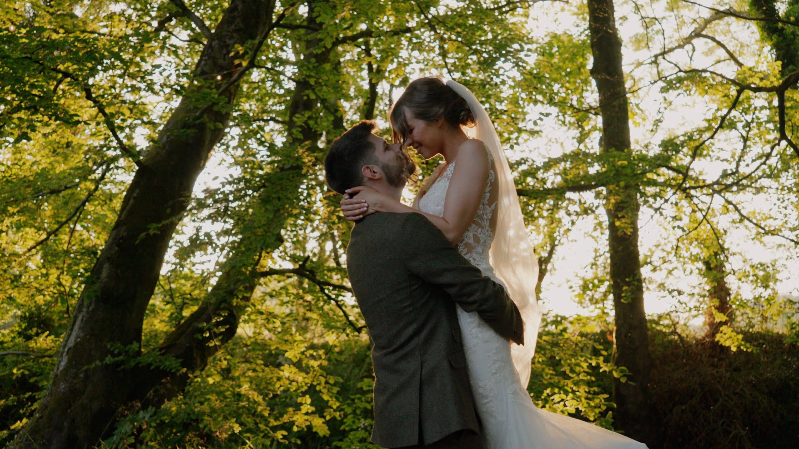 Bride and groom embracing in a forest setting during sunset.