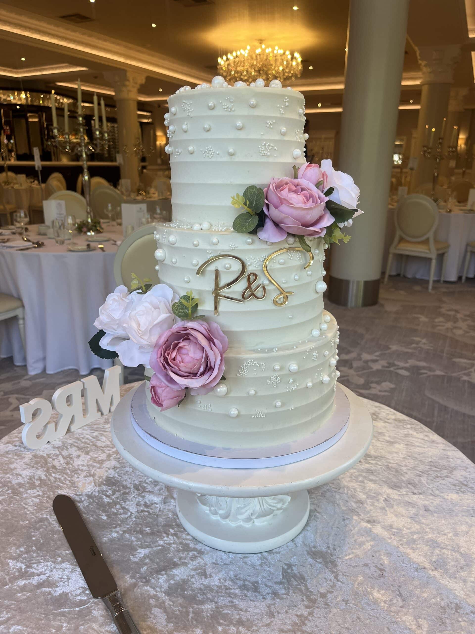 Elegant white wedding cake with floral decorations and initials "R & S" in a luxurious banquet setting.