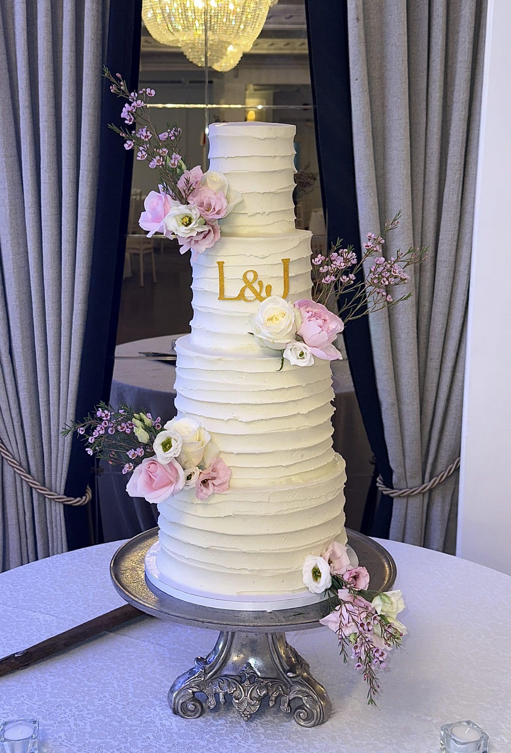 Elegant white wedding cake with floral decorations and initials "L & J," displayed on a silver stand.