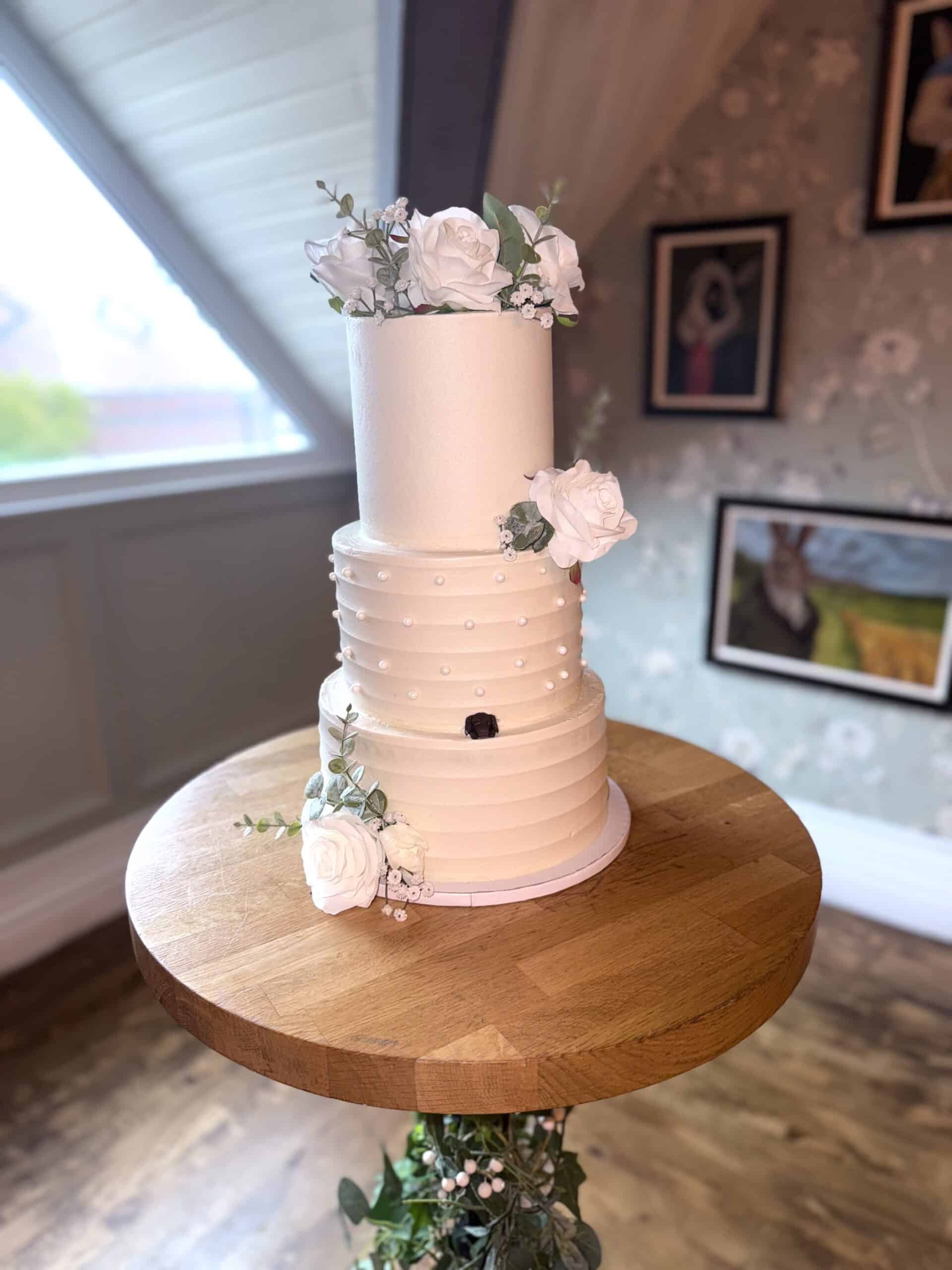 Elegant two-tier wedding cake with white roses on a wooden stand.