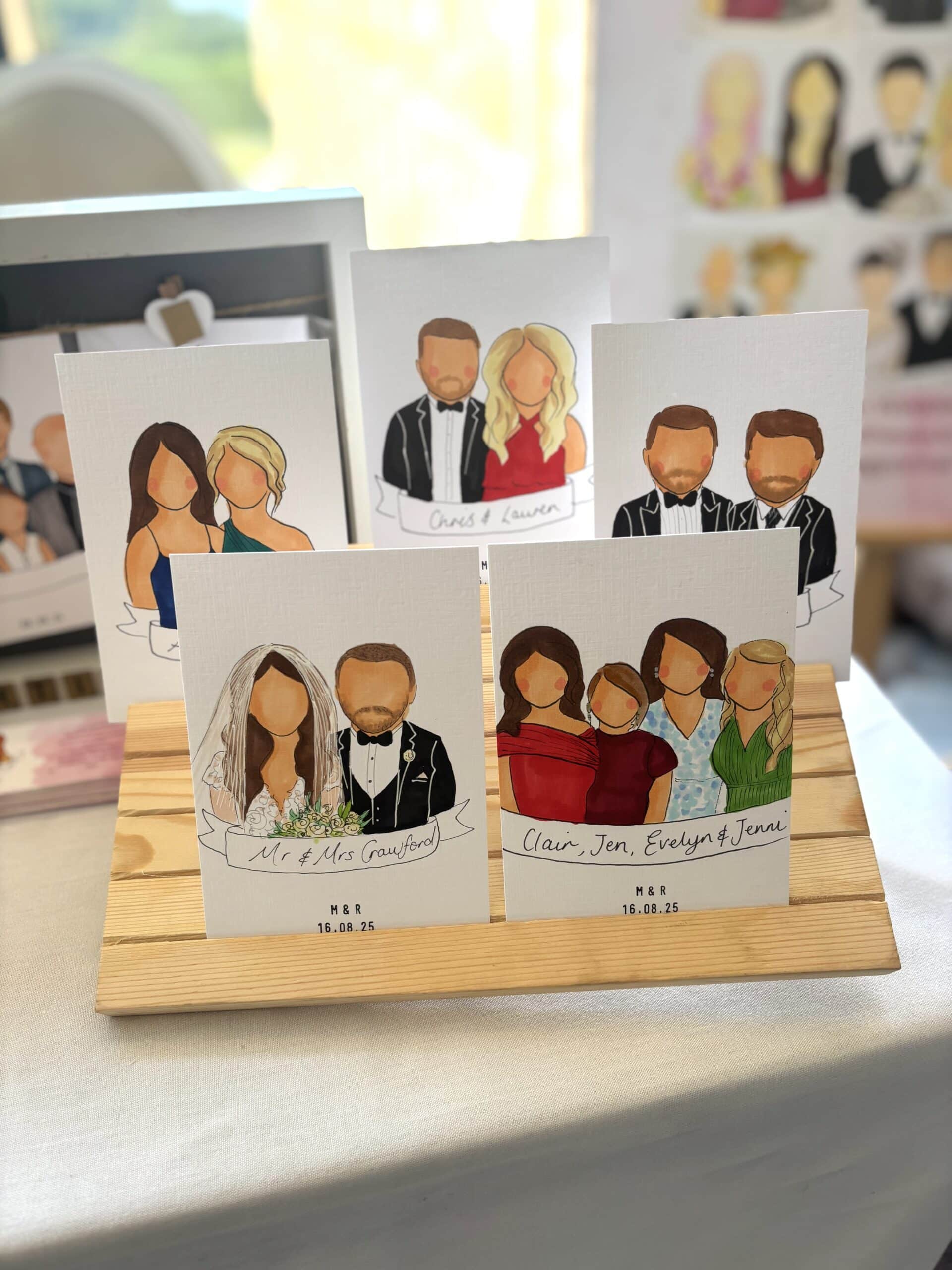 Illustrated wedding and group portraits on display, featuring faceless figures on a wooden stand.