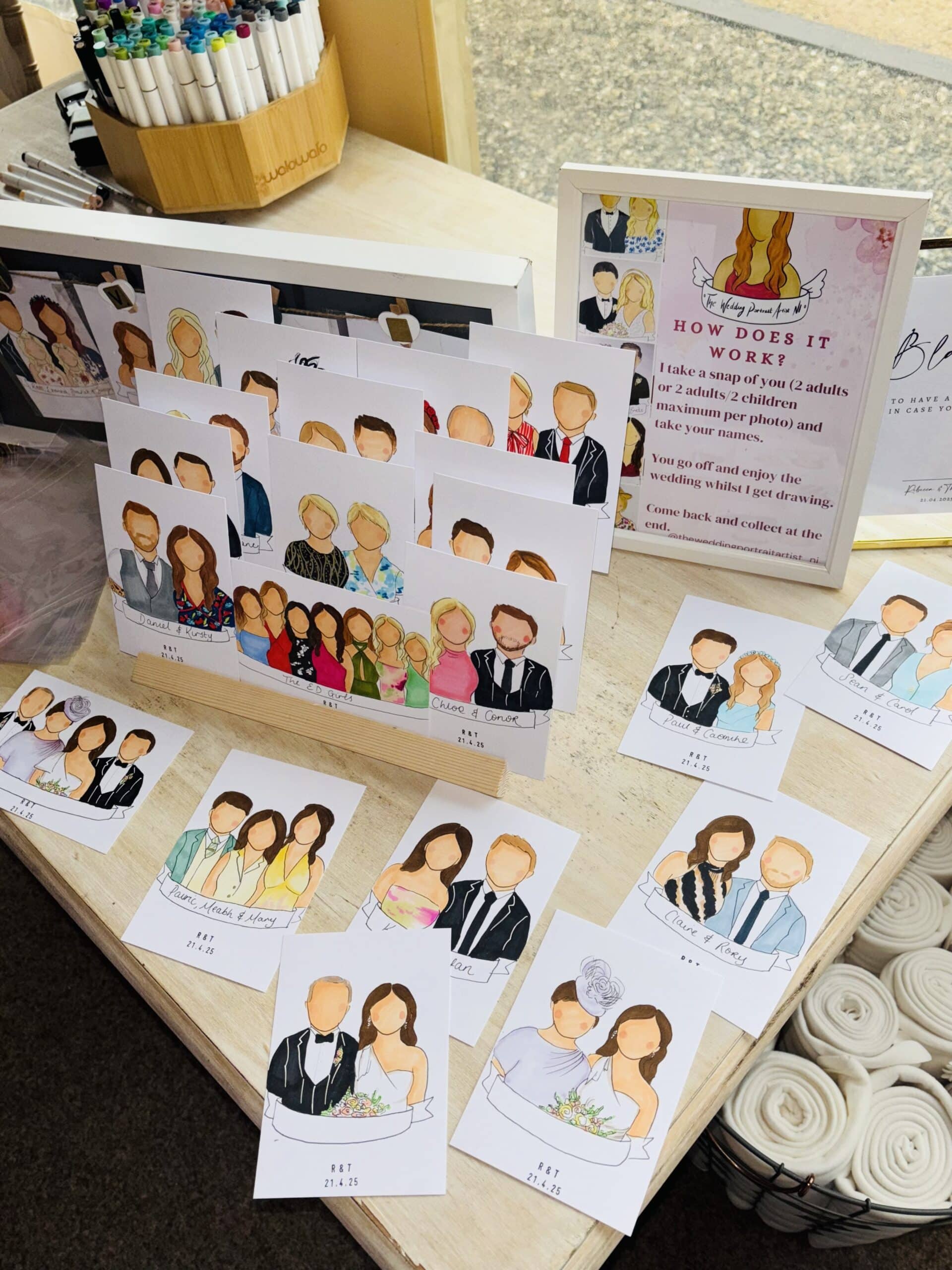 Custom wedding illustrations on display, showing various couples in colorful outfits with a framed instruction sheet nearby.