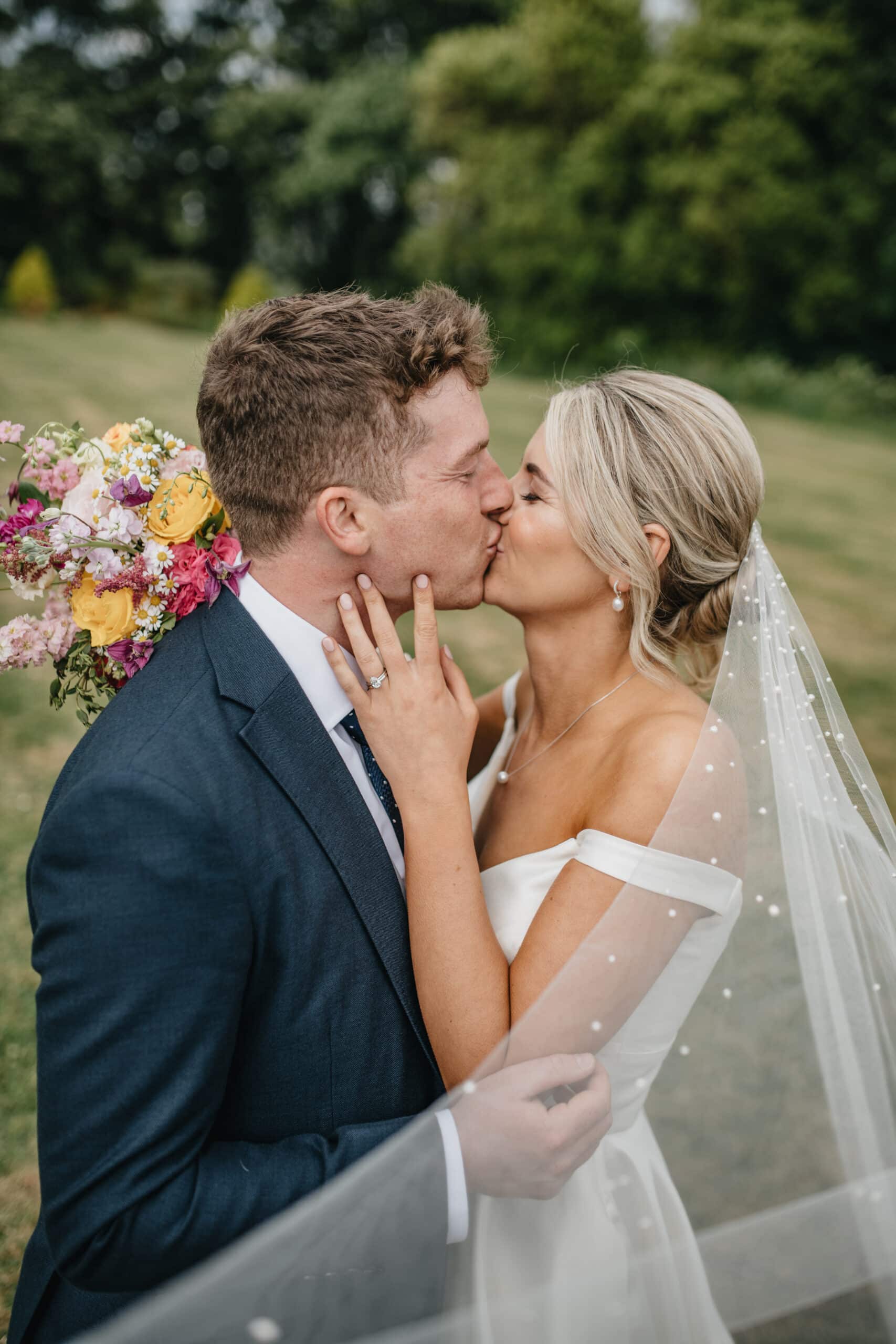Bride and groom kissing outdoors, bride holding colorful floral bouquet.