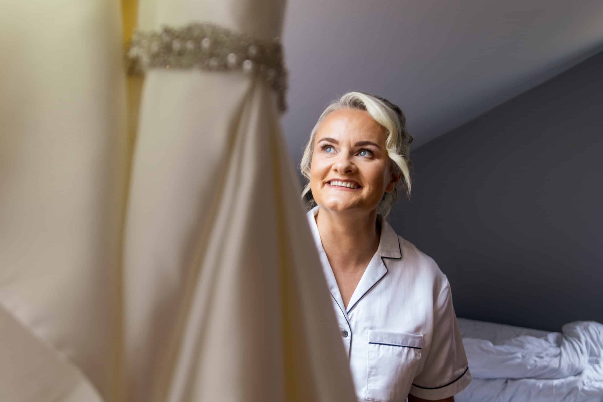 Woman smiles while looking at a wedding dress in a room.