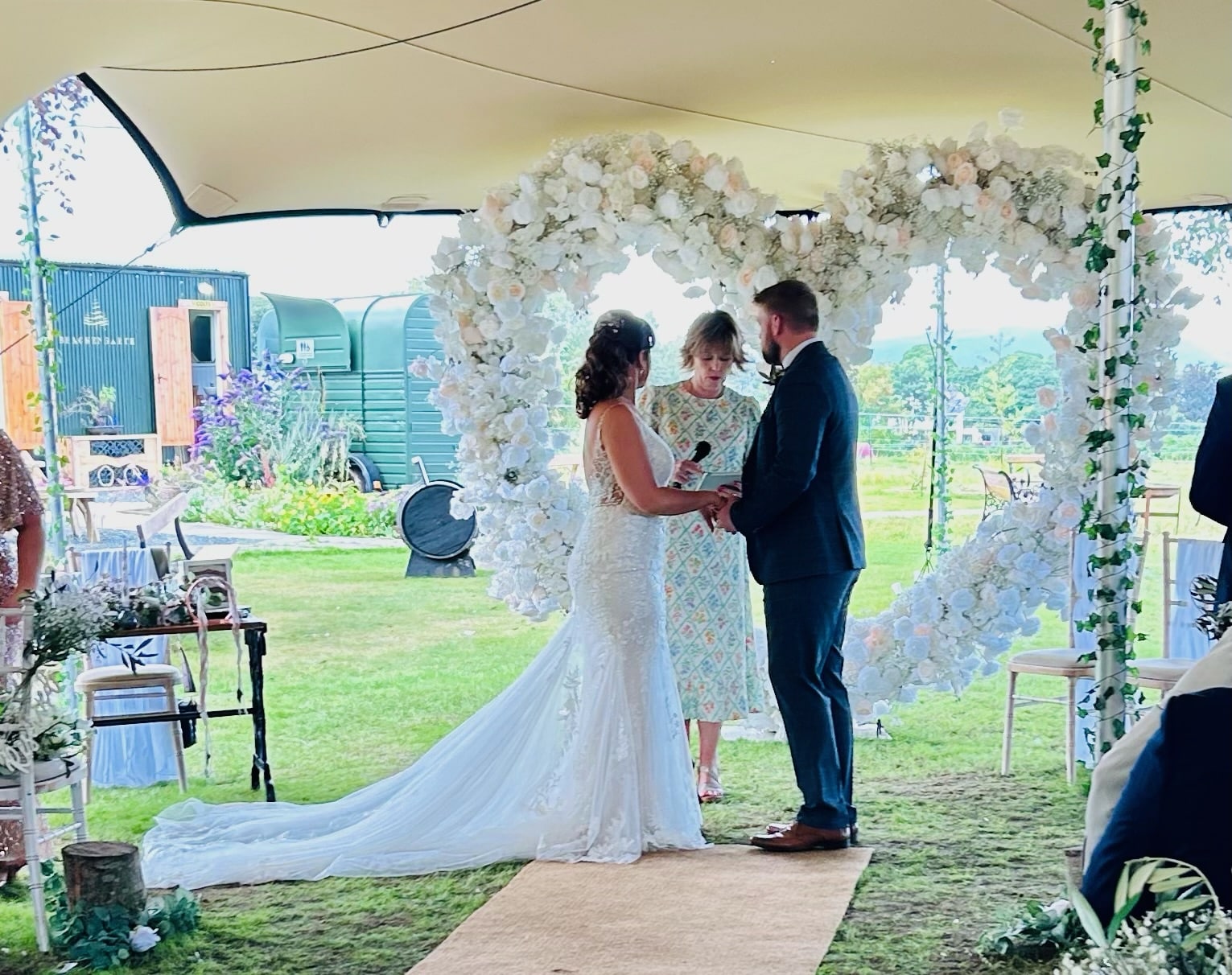 Bride and groom exchanging vows under a floral arch at an outdoor wedding ceremony.